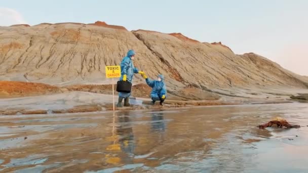 Filmagem completa de dois ambientalistas em trajes de proteção com equipamentos de coleta de material de águas residuais poluídas para análise química de área tóxica - Filmagem, Vídeo