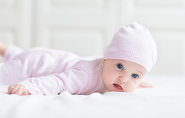Красивая маленькая девочка с большими голубыми глазами на белом одеяле играет на животе
 - Фото, изображение