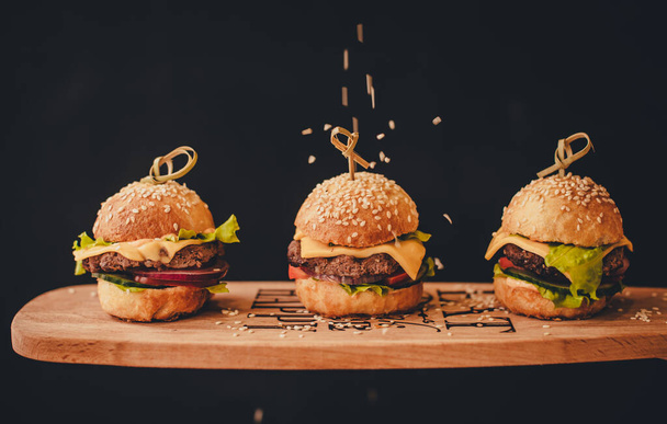 Three burgers on a wooden stand. Black background. - Foto, immagini