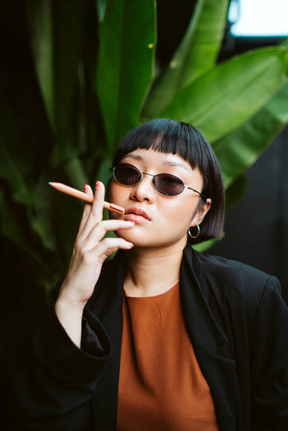 Raffreddare asiatico capelli corti donna indossare occhiali da sole tenendo penna come sigaretta. - Foto, immagini