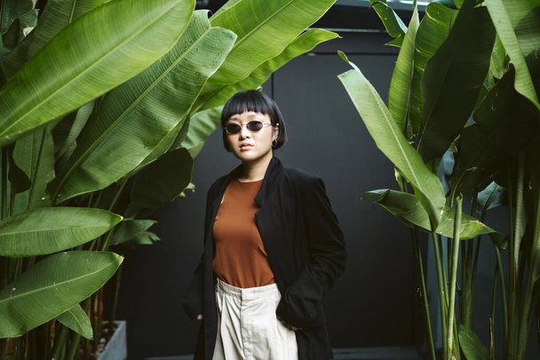 Retrato de jovem asiático cabelo curto mulher vestindo óculos de sol no jardim. - Foto, Imagem