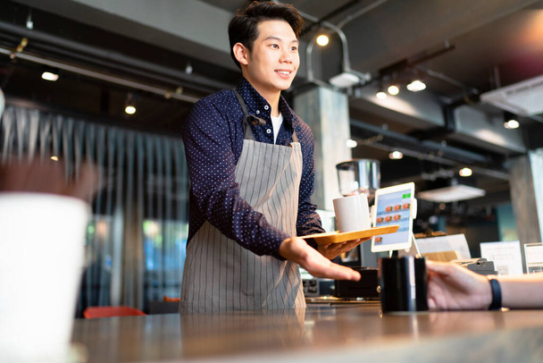 Ázsiai barista férfi forró kávét szolgál fel az ügyfélnek a kávézóban. - Fotó, kép