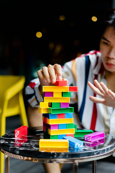 Молодой человек играет в разноцветную Дженгу с другом на вечеринке. - Фото, изображение
