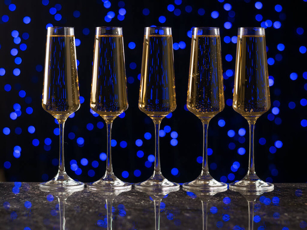 Cinco copos de vinho em pé ordenadamente sobre a mesa contra um fundo azul bokeh. - Foto, Imagem