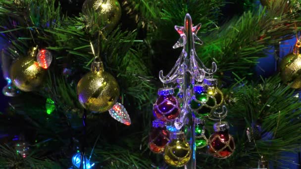 Kleine kerstboom versierd met peren op de achtergrond van een grote kerstboom versierd met bloemenslingers - Video