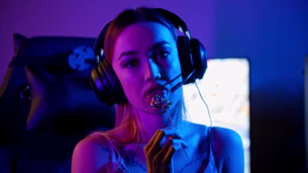 Tetovaný hráč dívka sedí u herního PC a sání lízátko - Záběry, video