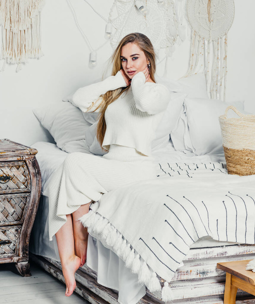 jovem mulher com cabelo loiro loiro de luxo longo na cama no quarto em tons brancos interior - Foto, Imagem
