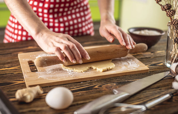 Woman is rolling out raw dough on a wooden table with a rolling pin to make delicious homemade cookies in her kitchen. - Fotografie, Obrázek