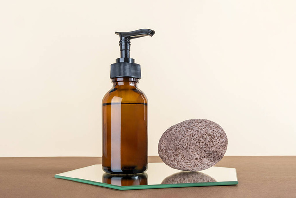 Brown glass bottle with pump of cosmetic products and stone on mirror, beige and brown background. Natural Organic Spa Beauty Cosmetic concept Mockup. - Foto, afbeelding