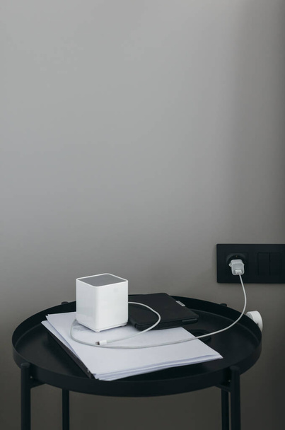 Modern black table with gadgets, portable speaker, e-book and charger. Contemporary interior style. Gray wall background, white accessories. - Photo, image