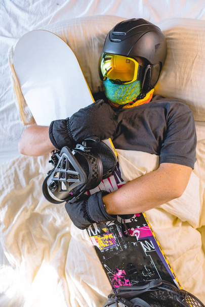άνθρωπος σε εξοπλισμό σκι κοιμάται στο κρεβάτι με snowboard - Φωτογραφία, εικόνα