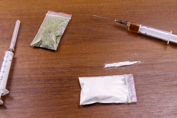 Różne rodzaje narkotyków: kokaina, strzykawka z heroiną i suszone konopie indyjskie na stole. Koncepcja zażywania narkotyków, przestępczości i uzależnienia - Zdjęcie, obraz