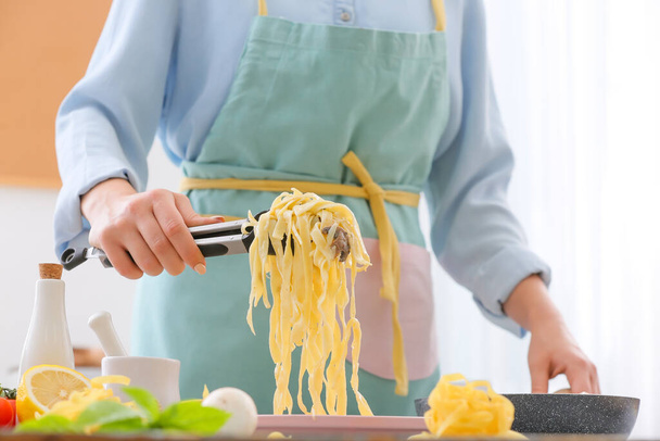 Женщина кладет макароны на тарелку на кухне - Фото, изображение