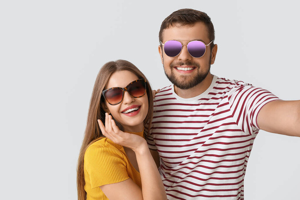 Jeune couple avec des lunettes de soleil élégantes prenant selfie sur fond clair - Photo, image