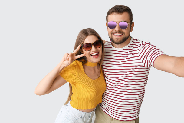 Молода пара зі стильними сонцезахисними окулярами приймає селфі на світлому фоні
 - Фото, зображення