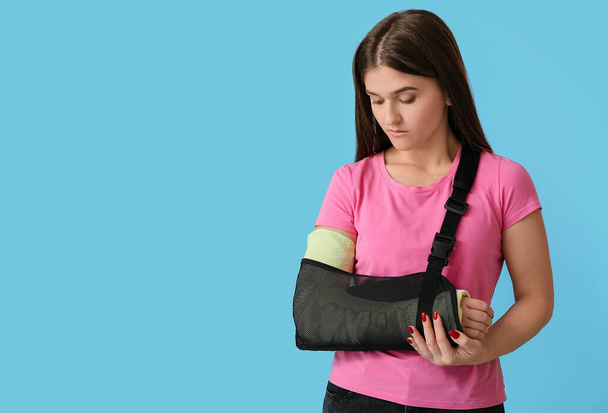 Mujer joven con el brazo roto en el fondo de color - Foto, Imagen