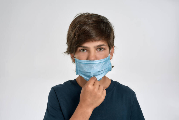 Portrait of little sportive boy child in sportswear wearing, adjusting medical mask, looking at camera, standing isolated over white background - Foto, Imagem
