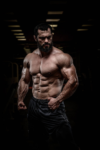 strong young bearded athlete male with perfect sport physique body torso muscle in dark fitness gym - Valokuva, kuva
