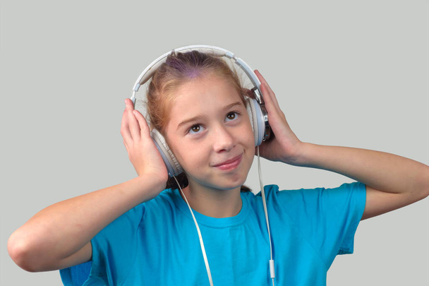 Ein braunäugiges Mädchen trägt Kopfhörer und hört Musik - Foto, Bild
