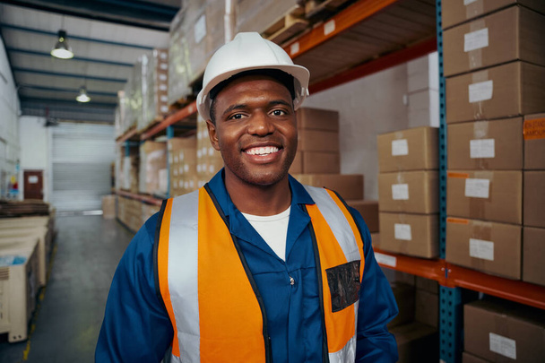 Retrato sorridente de um jovem trabalhador africano de chapéu branco e uniforme no armazém - Foto, Imagem