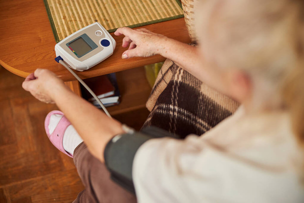 Oudere vrouw die thuis elektronische bloeddrukmeter gebruikt - Foto, afbeelding