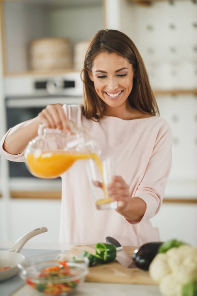 Снимок молодой женщины, пьющей свежий апельсиновый сок на кухне. - Фото, изображение
