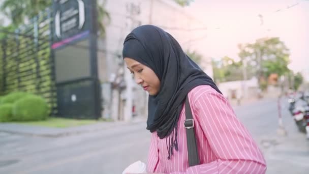 Houkutteleva väsymys aasialainen musliminainen, jolla on musta hijabi kävelemässä tien varrella kädet kädessä, vie pois kahvikuppi, uneton yö, nuori aikuinen työntekijä, joka kävelee toimistoon liikealueella, moderni teknologia ja matkamuistot. - Materiaali, video
