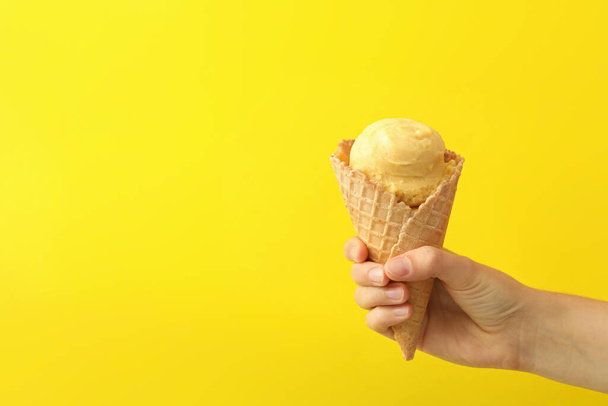 Mujer sosteniendo cono de gofre con delicioso helado sobre fondo amarillo, primer plano. Espacio para texto - Foto, imagen