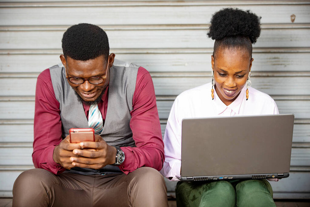 Dwóch afrykańskich biznesmenów szukających informacji na stronie telefonu komórkowego, siedzących przy stole z laptopem i... Koledzy sprawdzają maile na komórce. - Zdjęcie, obraz