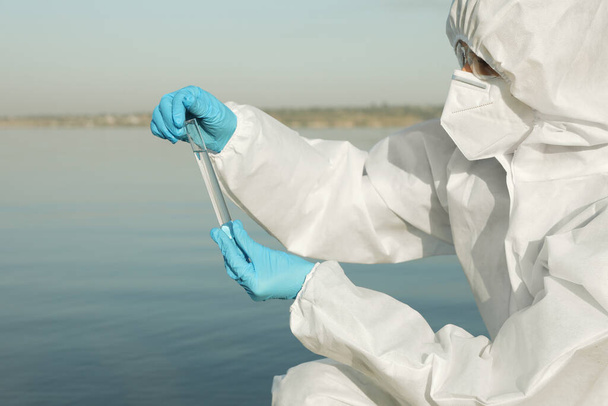 Вчений в хімічному захисному костюмі з пробіркою, взявши зразок з річки для аналізу
 - Фото, зображення