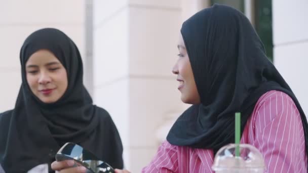 deux y femmes musulmanes asiatiques portent hijab sur leur pause café après-midi montrant écran de smartphone à son ami, assis à l'extérieur du café, la mise en ligne de photos, réunion d'amis heureux et rires, connexion Internet sans fil, la vie religieuse moderne - Séquence, vidéo