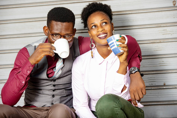 Mutlu ve güzel Afrikalı çift birlikte oturup gülümserken bir fincan kahve içiyorlar. - Fotoğraf, Görsel