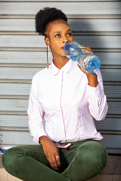 молодая деловая женщина, сидящая снаружи и пьющая воду в бутылке. - Фото, изображение