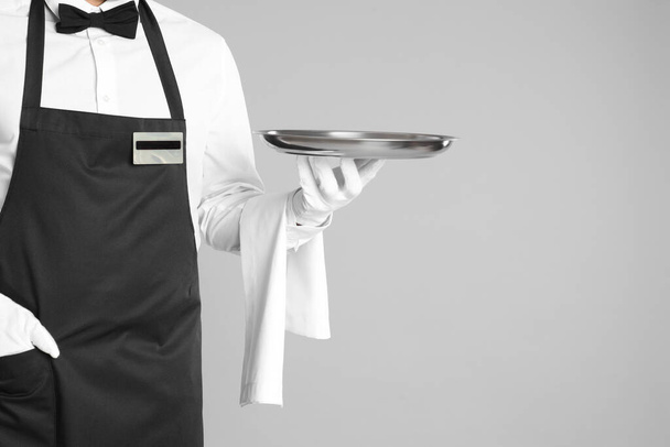 Waiter holding tray on light grey background, closeup. Space for text - Zdjęcie, obraz
