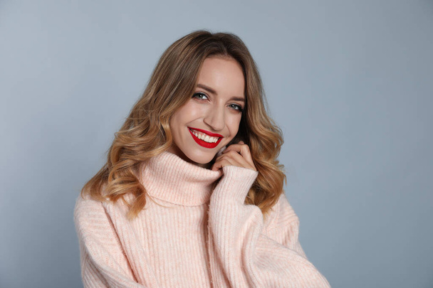 Happy young woman wearing warm sweater on grey background. Christmas celebration - Foto, imagen