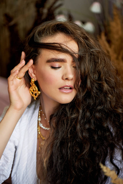 A beautiful girl with long hair corrects curls. Thick eyebrows. Model appearance - Fotó, kép