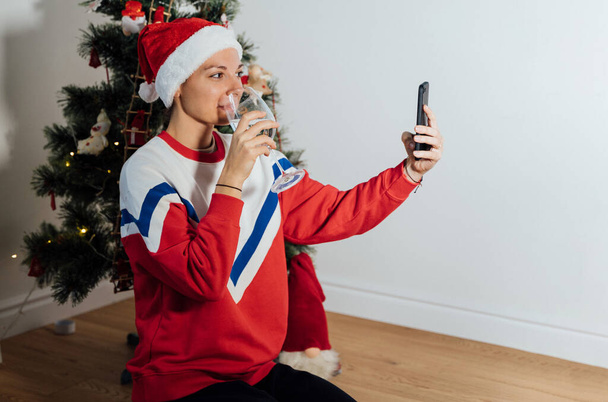 Mujer joven del milenio usando el teléfono en casa en Nochebuena. Compras de vacaciones en línea, cuarentena celebración virtual  - Foto, Imagen