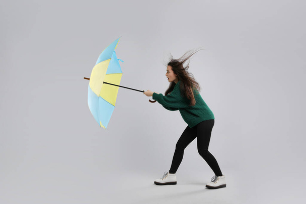 Emotional woman with umbrella caught in gust of wind on grey background - Photo, image