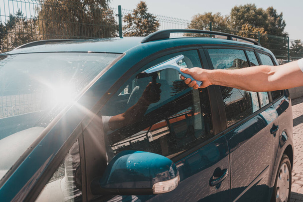 Adam oto yıkamada arabayı yıkadıktan sonra bardaktan su kalıntılarını alıyor, araba mavi. 2020 - Fotoğraf, Görsel