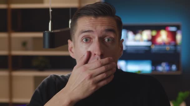 Close-up portret van een bange man uitpuilende ogen en bedekken mond in angst reageren op verschrikkelijke situatie op kantoor thuis appartement achtergrond in de avond - Video