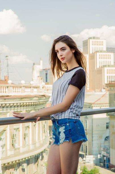 Chica en pantalones cortos de mezclilla en el balcón. Retrato de verano de una joven hipster con estilo posando en el balcón - Foto, imagen