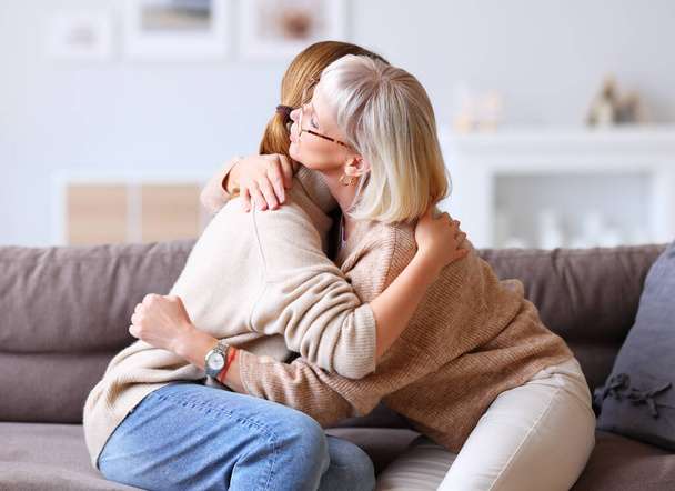Vista lateral de la mujer mayor abrazando y reconfortante hija molesta mientras se sienta en el sofá en hom - Foto, Imagen