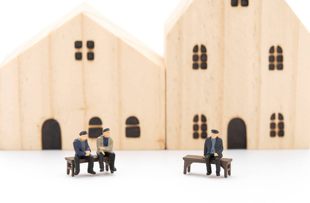 Minyatür adamlar bankta oturup birbirleriyle konuşuyorlar, evin arka planı bulanık.. - Fotoğraf, Görsel