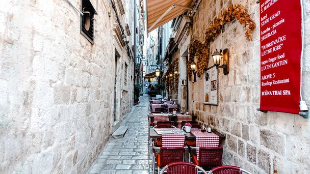 The cafe scene in Dubrovnik Croatia. Narrow cobblestone street with a cafe and outdoor seating - Foto, afbeelding
