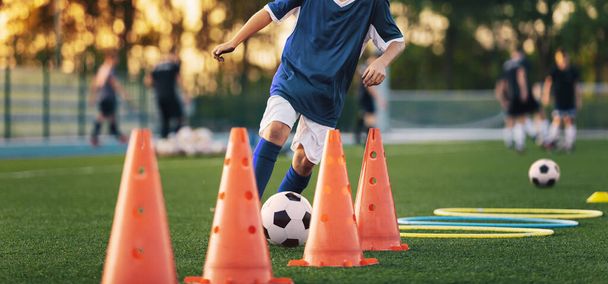 Football Player on Training Szlalom fúró labdával. Futball fiú között futó piros gyakorló bóják füves gyakorlótéren - Fotó, kép