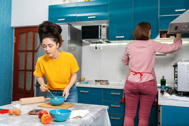 Dos mujeres jóvenes cocinan en la cocina usando recetas en línea en un teléfono inteligente. Concepto de cocina en casa, parejas LGBT. - Foto, Imagen