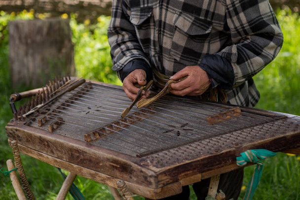 Κίεβο, Ουκρανία - 12 Μαΐου 2019: Ένας ηλικιωμένος Ουκρανός ένας χωρικός με μακρύ μουστάκι και γενειάδα παίζει ένα αρχαίο μουσικό όργανο από κύμβαλα. Vintage χωριό με ξύλινα σπίτια. Μουσείο Πιρόγκοβο - Φωτογραφία, εικόνα