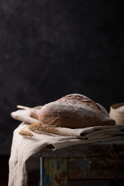 Φρέσκο σπιτικό ψωμί σε σκούρο φόντο, με λιναρόσπορους σε αλεύρι ολικής αλέσεως. Γαλλικό ψωμί στρογγυλό σχήμα. Ψήσιμο ψωμιού Ψωμί χωρίς λοβό - Φωτογραφία, εικόνα