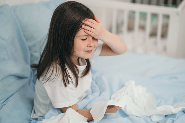 The child has a cold and is being treated at home. The girl has a headache. The child is ill and lies in bed - Фото, изображение