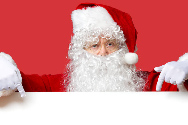 Santa Claus mirando por detrás de la pizarra blanca en blanco aislado sobre fondo rojo con espacio de copia - Foto, imagen
